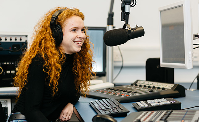 Female student sat at radio studio desk, wearing headphones